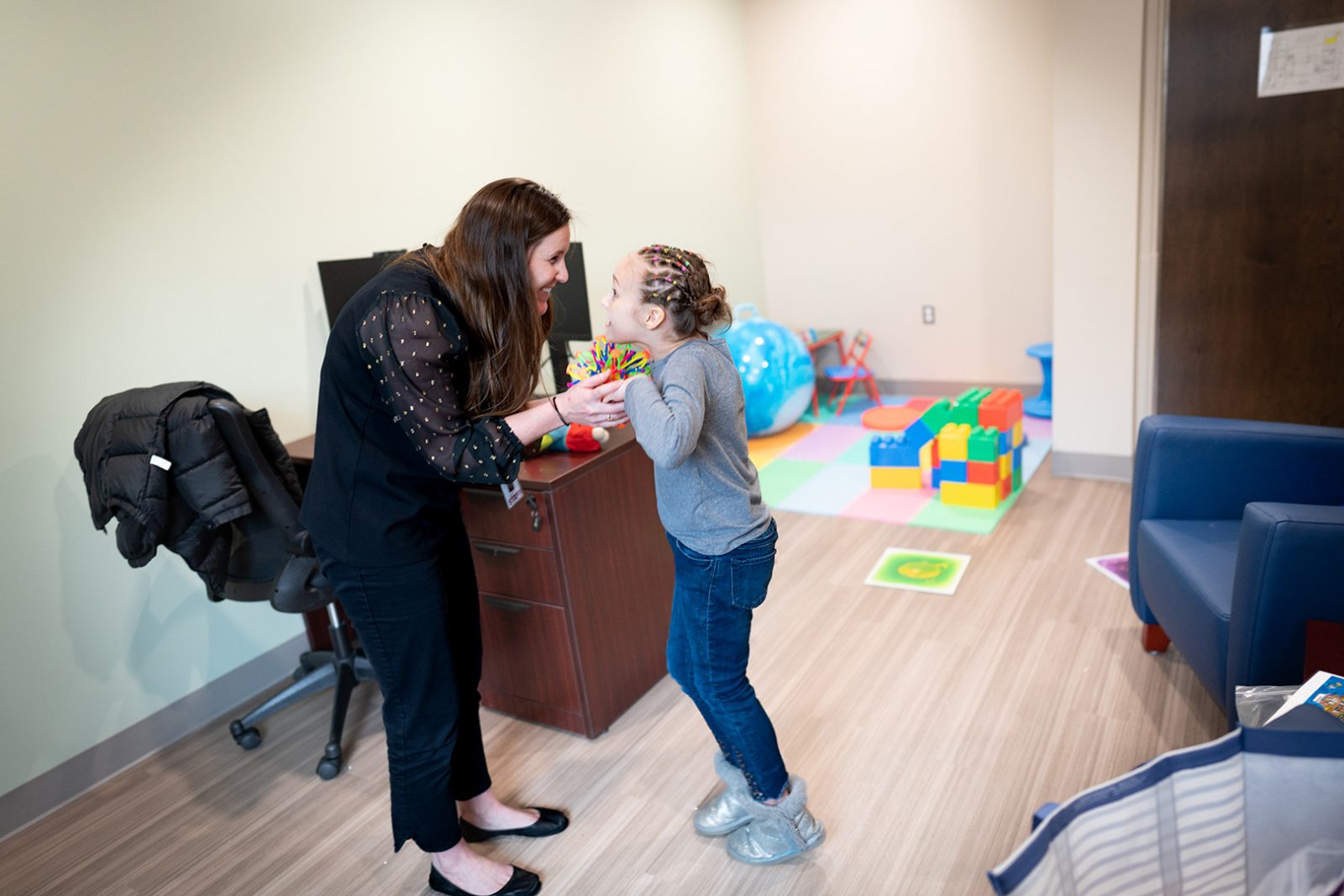 An autism assessment specialist leans in to hold the hands of an excited girl during structured play in an autism assessment test.