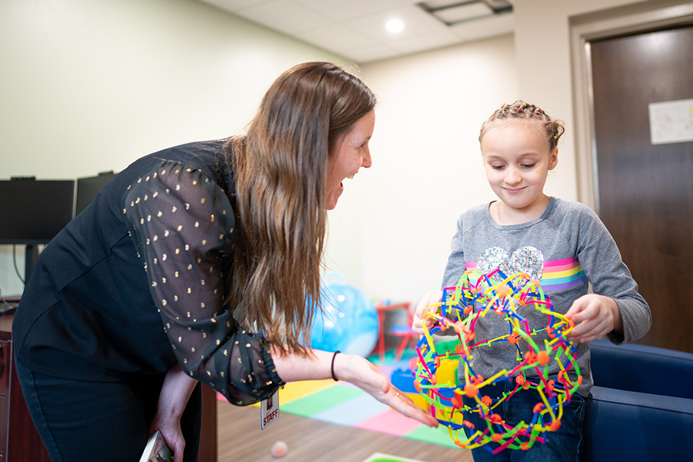 A smiling medical professional working with a young female autism patient holding a colorful plastic interlocking toy.