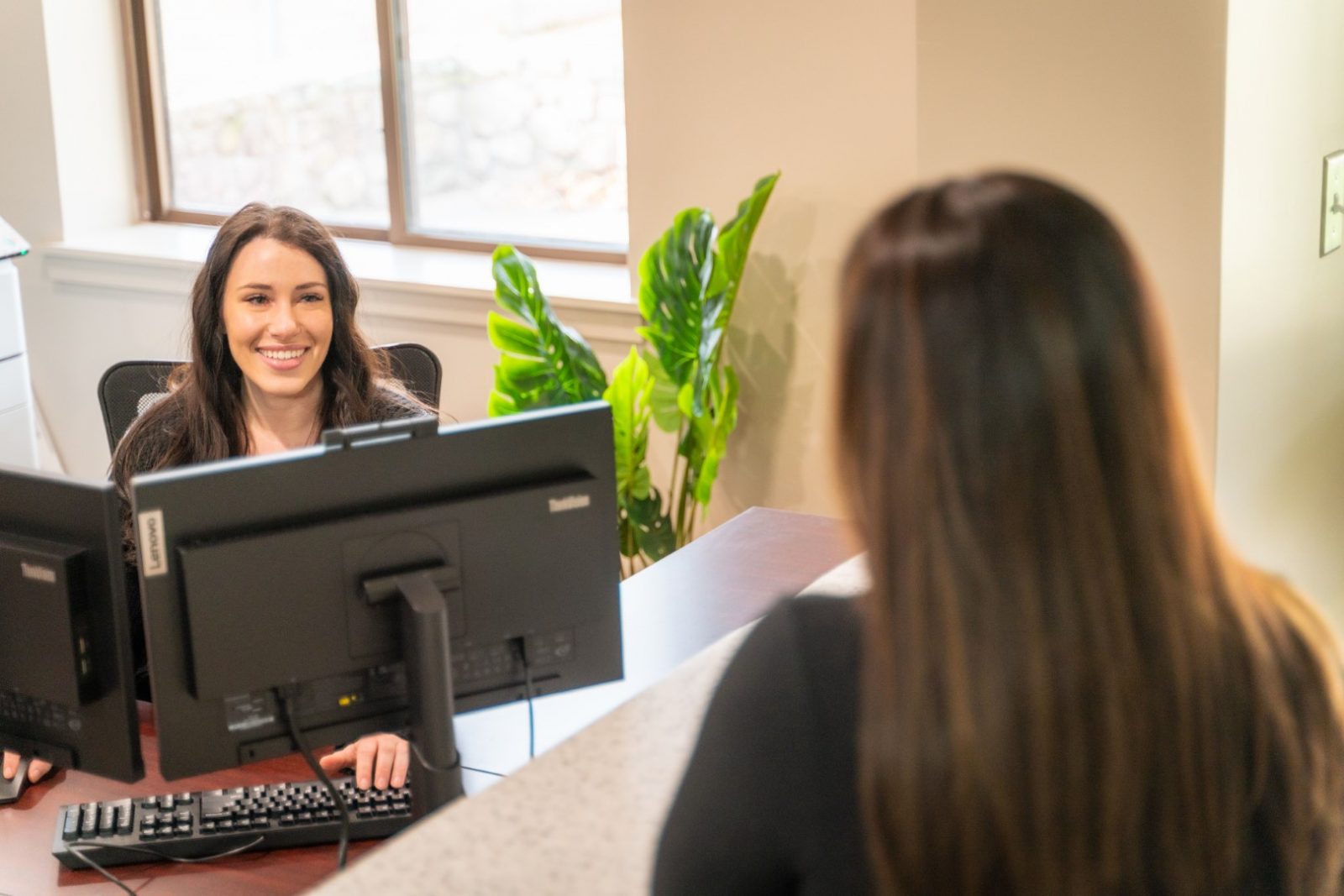 Staff member at a desk at a behavioral health center smiles at a client as she schedules her consultation with medication doctors.
