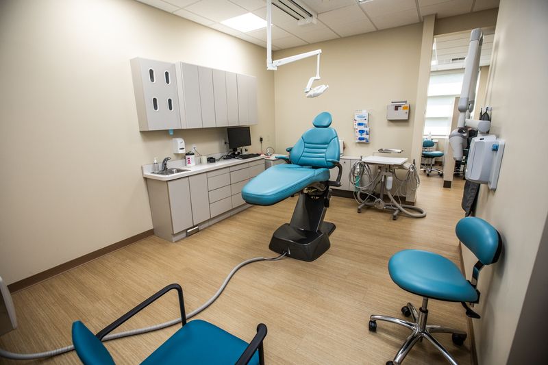 A spacious dental office with blue chairs, overhead lamp, and dental equipment at Penn Dental Medicine at Woods. 