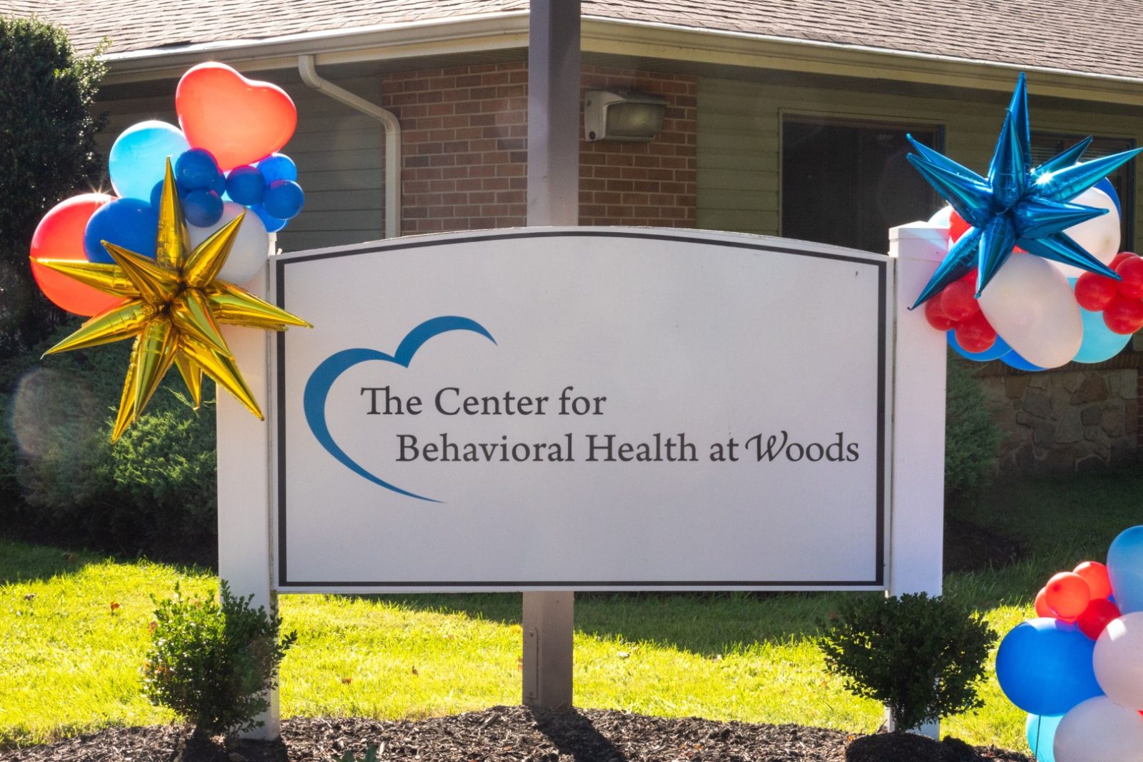 Sign for The Center for Behavioral Health at Woods, a site of inclusive healthcare, decorated with balloons.